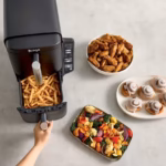 Ninja DoubleStack 2-Basket Air Fryer SL201C on a counter with fries in the open basket, a bowl of wings and a tray of roasted vegetables