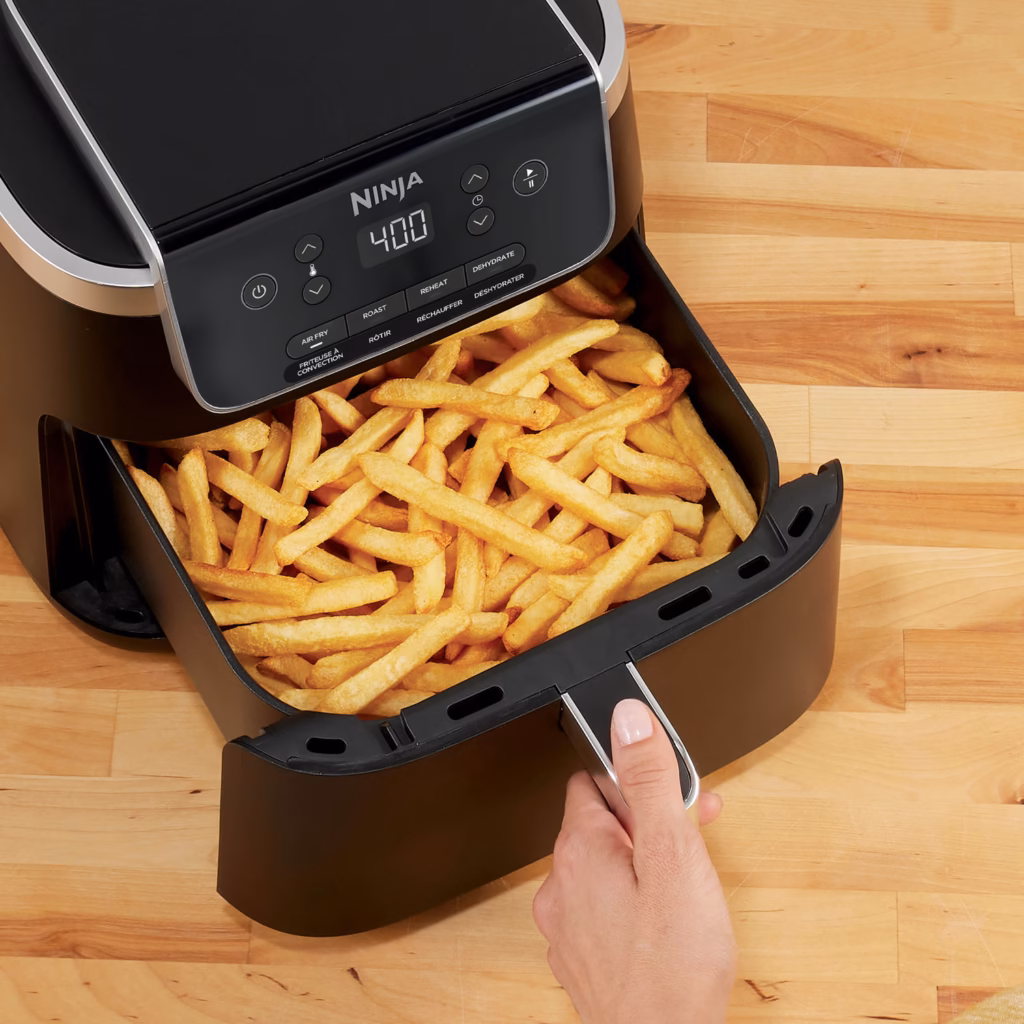 Ninja AF141C air fryer drawer being pulled out by hand, loaded with fries