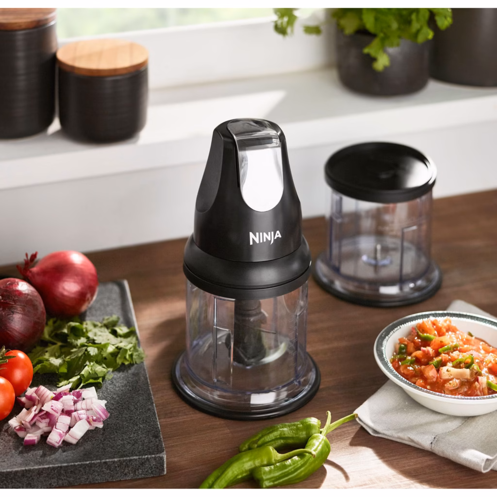 Ninja NJ100C Express Chop on a kitchen counter beside its bowl fitted with the splash guard storage lid