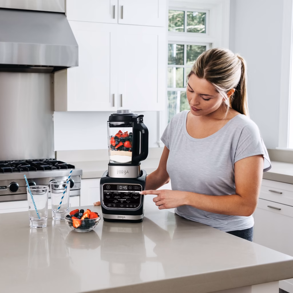 Ninja HB150C blending a berry smoothie in its glass pitcher in a bright kitchen