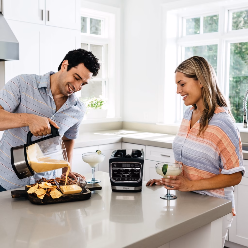 Ninja HB150C pouring hot blended queso dip from the glass pitcher onto a snack board